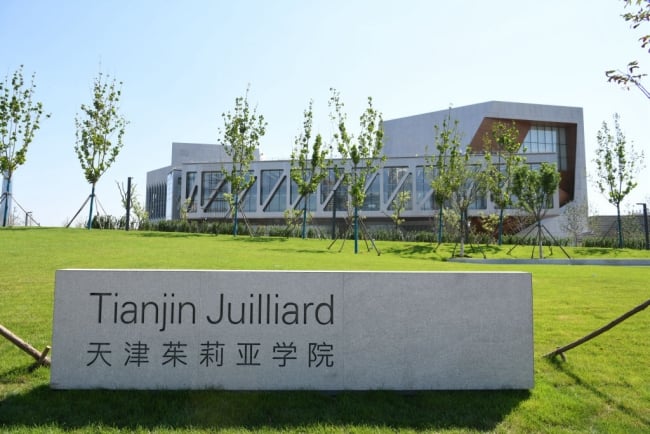 A campus in a green lawn with a sign that says Tianjin Juilliard in English and Chinese.