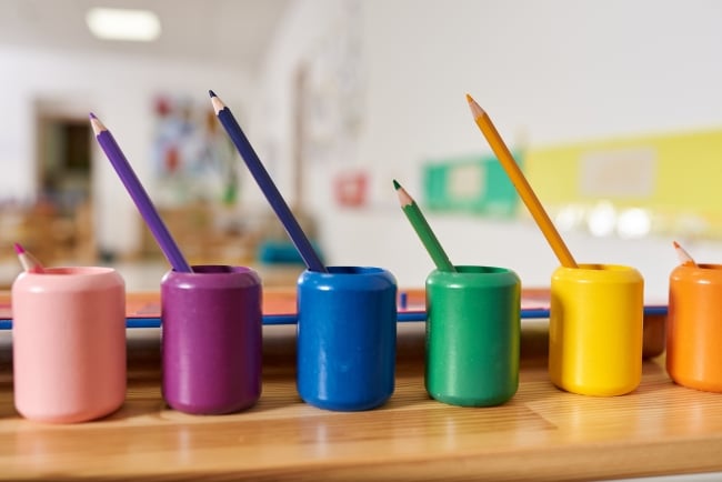 6 colorful Montessori pencil holders in foreground of blurred classroom (opinion)