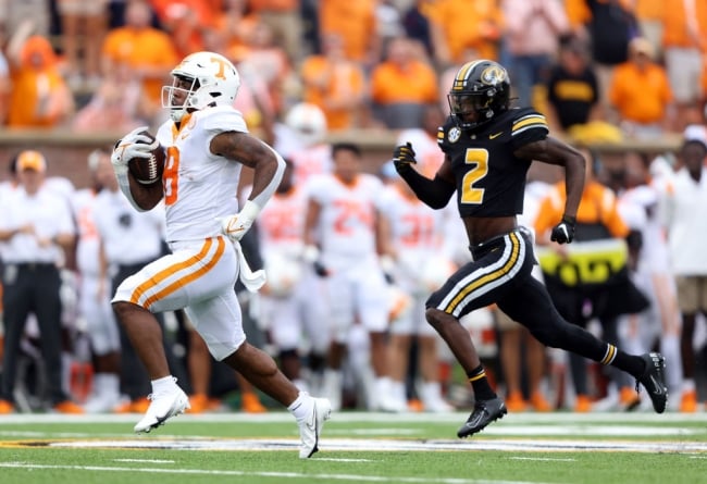 Two football players running, one in front with a ball.