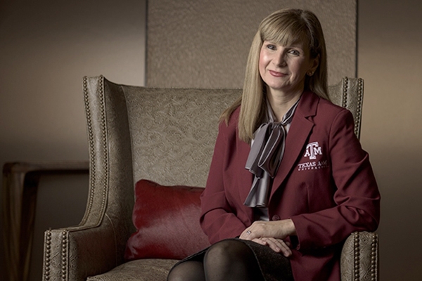 A photograph of a woman sitting, wearing a maroon blazer with the Texas A&M University logo on it.