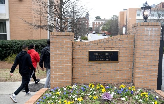Three students walk past a plaque on a brick wall that reads "Morehouse College, founded 1867."