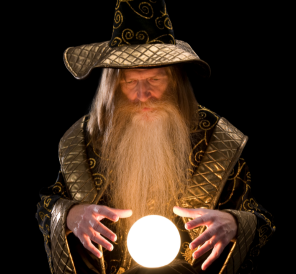 A wizard, dressed in a robe and pointy hat, stands with his hands hovering above a glowing crystal ball.