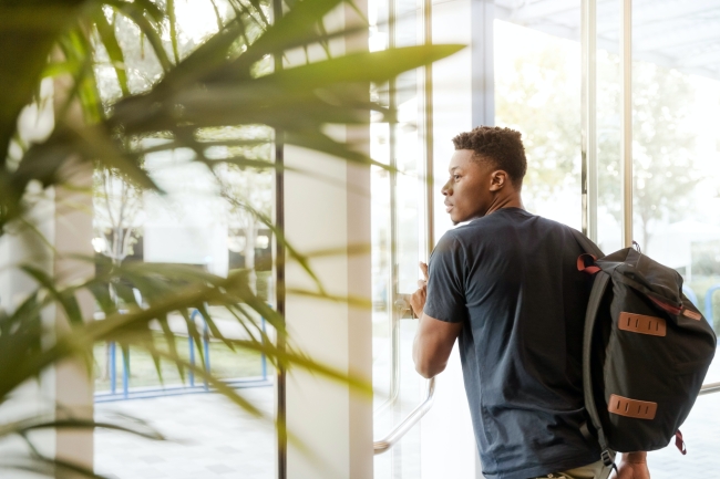 A Black male student carries a backpack as he exits a building.