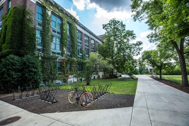 Photo of a college campus in Syracuse, N.Y. Bikes are on a bike rack in front of a brick building covered in picturesque ivy.