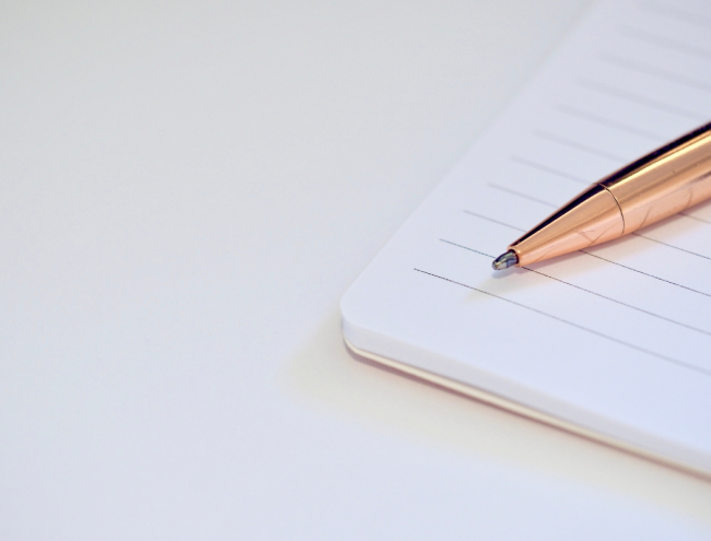 An orange pen rests on a blank sheet of white lined paper.