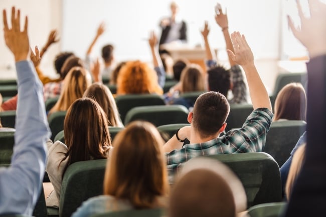 Students raise their hands in a college classroom.