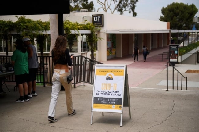 A woman walks past a yellow and white sign advertising a vaccine clinic.