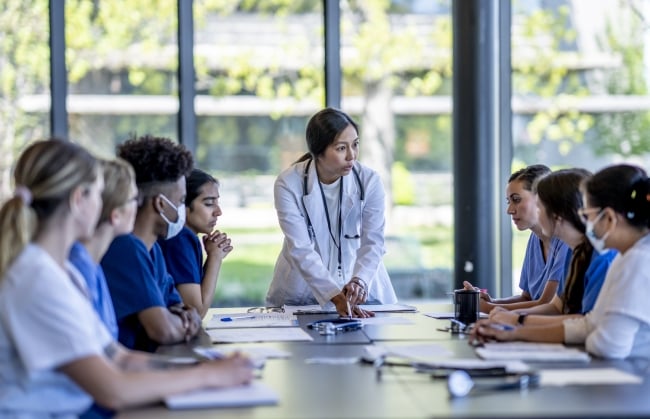 A group of nursing students sits around a long conference table looking at the instructor