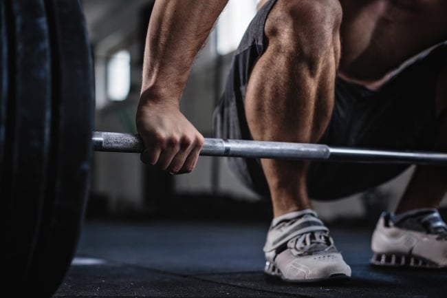 Legs and arm of a man lifting a heavy barbell in a gym