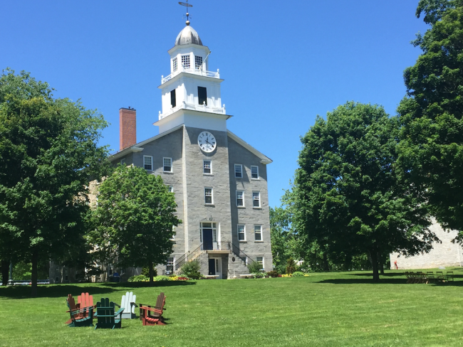 Middlebury's stone chapel in front of a blue sky. In the foreground, lawn chairs sit in a circle on the grass.