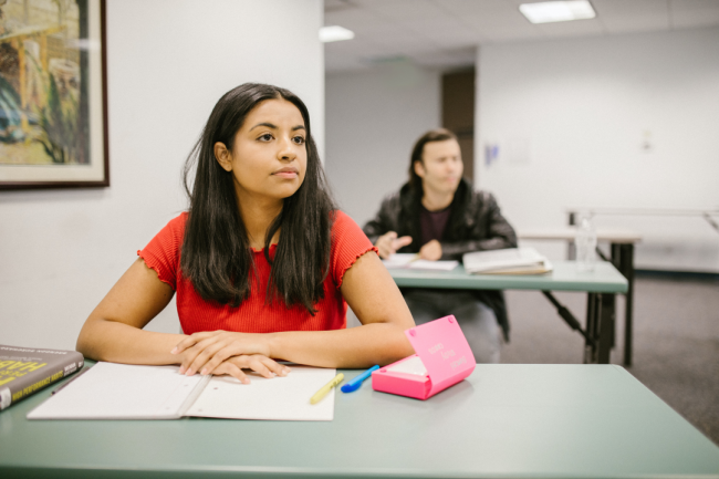 Two students sit at their desks with notebooks open.