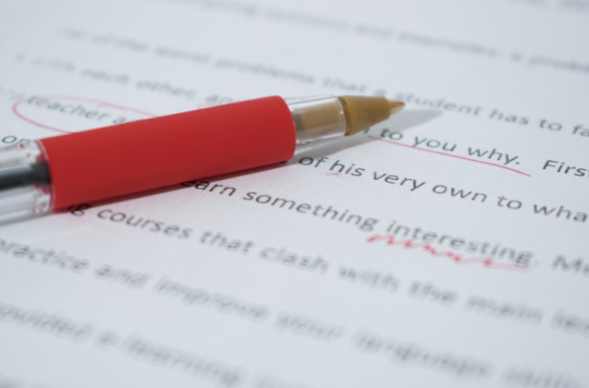 A red pen rests on a marked-up English-language manuscript.