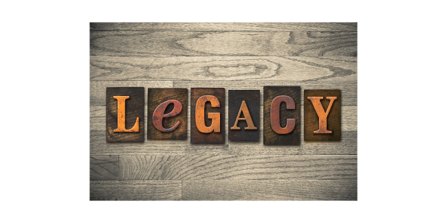 Six blocks with the letters spelling "LEGACY," in orange, atop a wooden table.