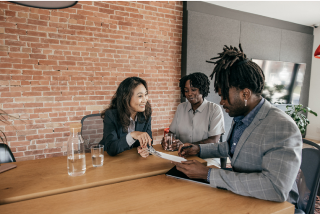 Three professionals representing different races talk in a corporate conference room.