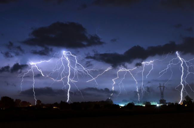 A photo of a thunderstorm—multiple storm clouds and lightning bolts can be seen against a dark blue/black background.