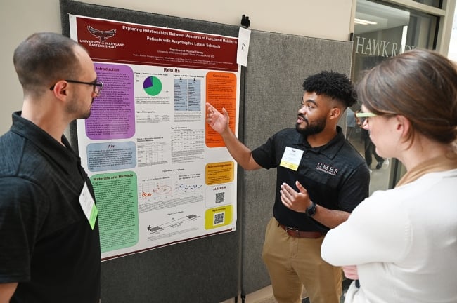 A physical therapy doctoral student at the University of Maryland Eastern Shore points to a poster with data and diagrams on it. 