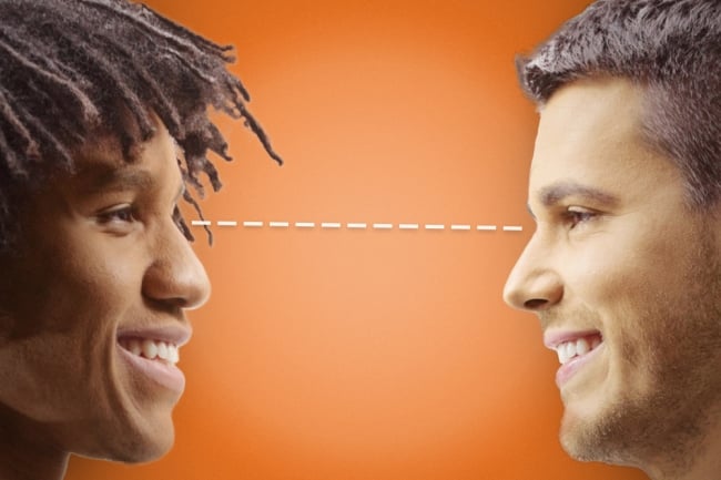 A young Black man making eye contact with an older white man against an orange background
