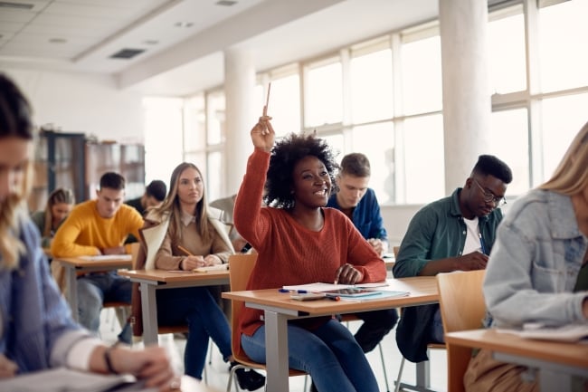 Black student raising hand to answer question while attending class with her university colleagues.