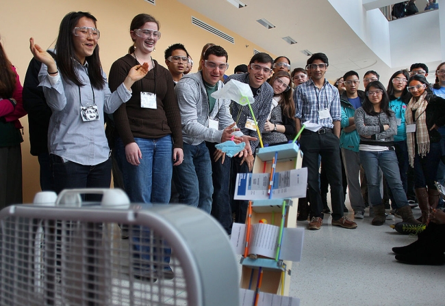 A group of students wearing lab goggles looks on excitedly at a homemade robot