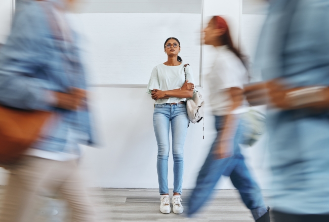 A young woman stands by herself while other people rush by her.