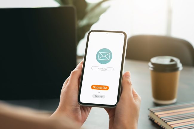 Two hands holding a smartphone with an email icon and subscription button.