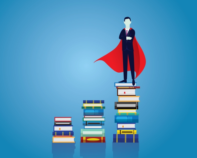 Man in a suit and a superman cape standing on a stack of books with two other stacks to the side of him