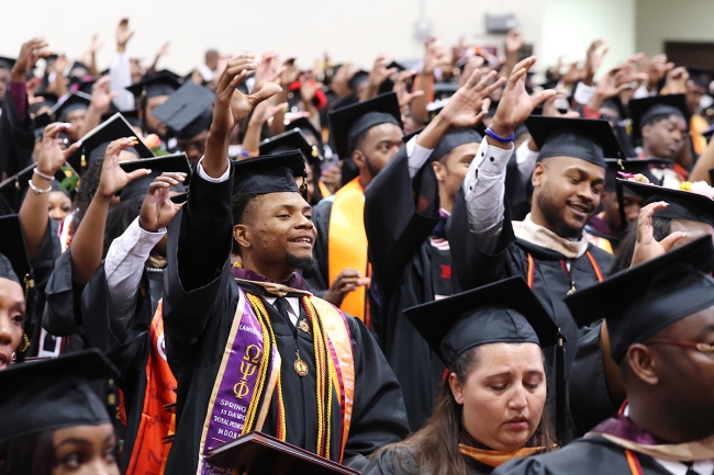 Graduates at Claflin University sit with hands raised in their graduation gowns and hats.
