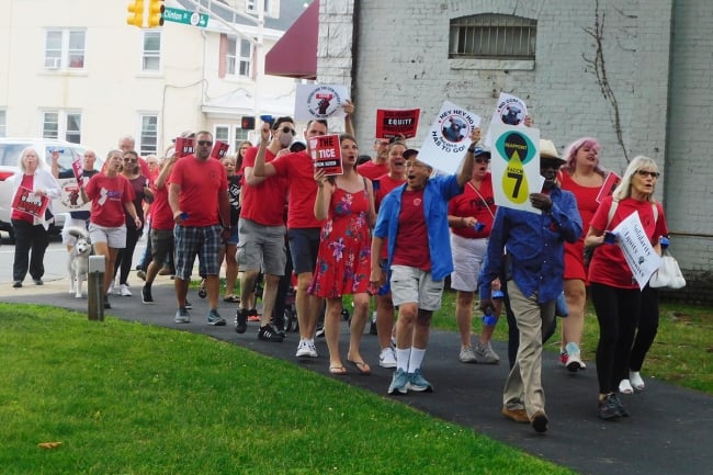 Professors in red Faculty Association shirts march holding signs. 