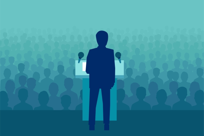 Man standing at podium in front of a crowd of heads without faces fading into background