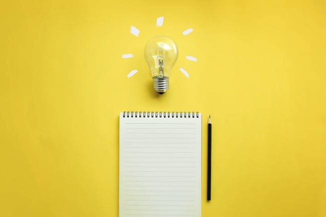 Pad of paper and pencil on a yellow background with a bright light bulb above them