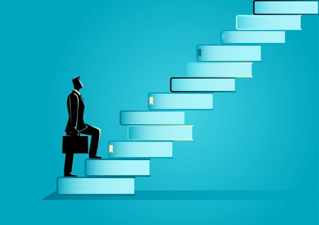 Man with a briefcase walks up a staircase of books