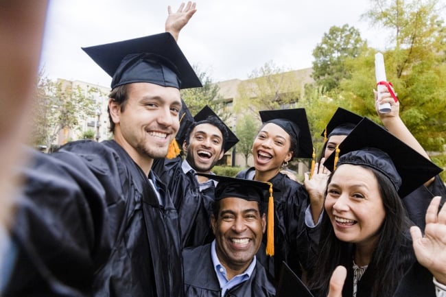 A group of college graduates smile for a selfie.