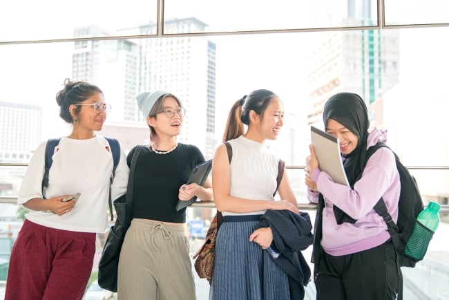 A group of four young Asian or Asian American women of diverse ethnicities standing in an academic building. 