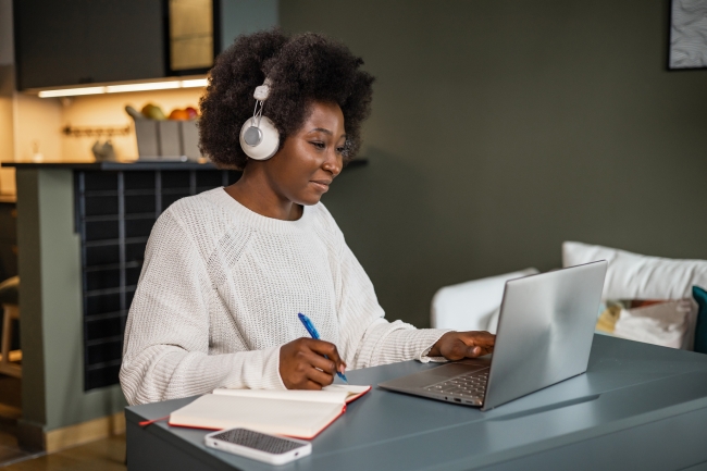 Young African American woman watching online course and writing notes