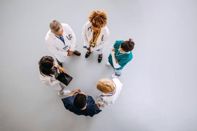 Five health-care professionals are seen from above, collaborating.