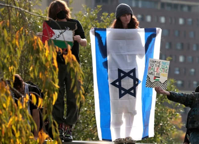 Three protesters, one for Israel and two for Palestine, stand by greenery.