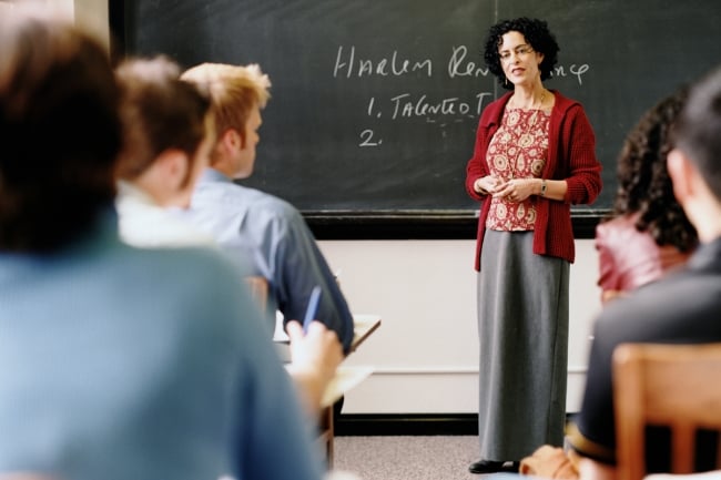 Female professor stands in front of chalkboard with the words "Harlem Renaissance" written on it.