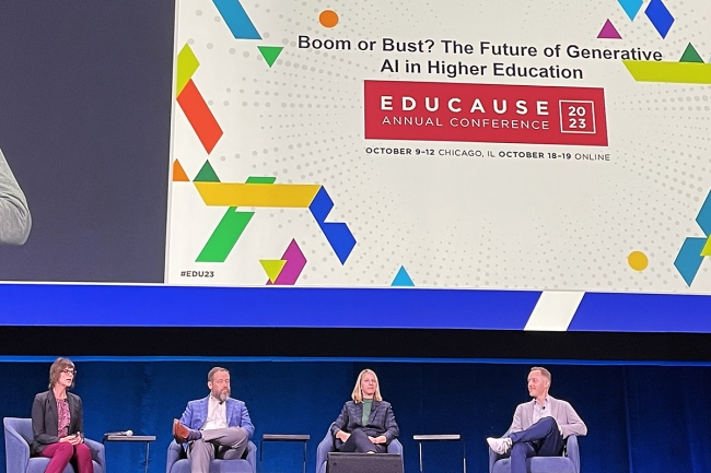 A group of panelists - two women, two men - sit on a stage in a line at a conference. The Educause logo is behind them. 