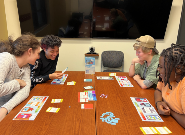 Four students play a board game on a brown table