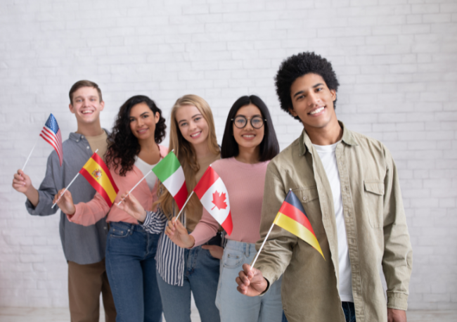 A group of five college-aged students holding flags from five different nations.