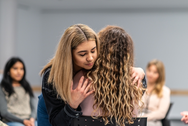 Two students hug and comfort each other during a support group session.