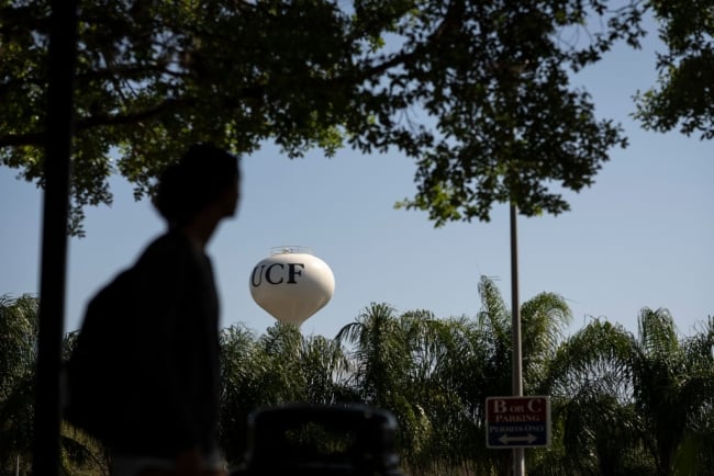 A water tower with the letters "UCF" on it sits in the distance; there is a blurry silhouette of a person in the foreground.