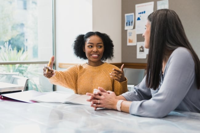 A female students gestures to a female career counselor seated next to her in an office space.