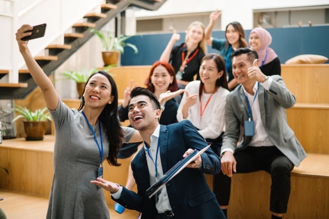 A group of students wearing professional clothing, with badges, takes a selfie in a campus-looking building. 