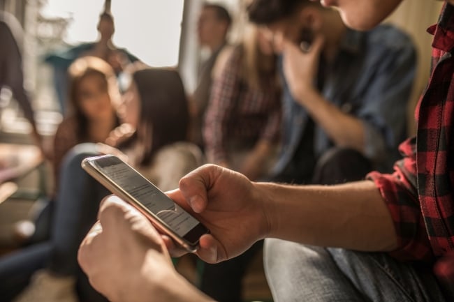 Unrecognizable male student text messaging on mobile phone while on a break in the classroom.