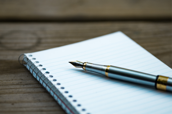 A fountain pen atop a blank notebook.