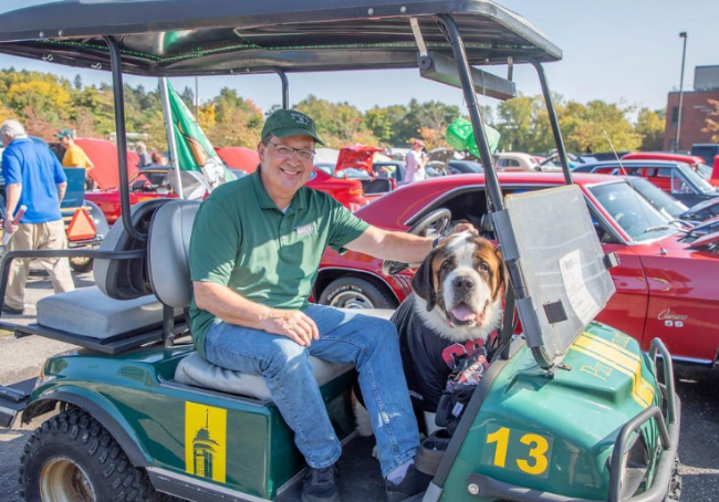 President Chuck Seifert sits in a green golf cart with school mascot, Baloo.