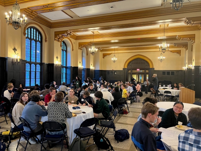 Sophomore students at Carleton College attend a banquet dinner, sitting at round tables with white tablecloths in a large meeting space.