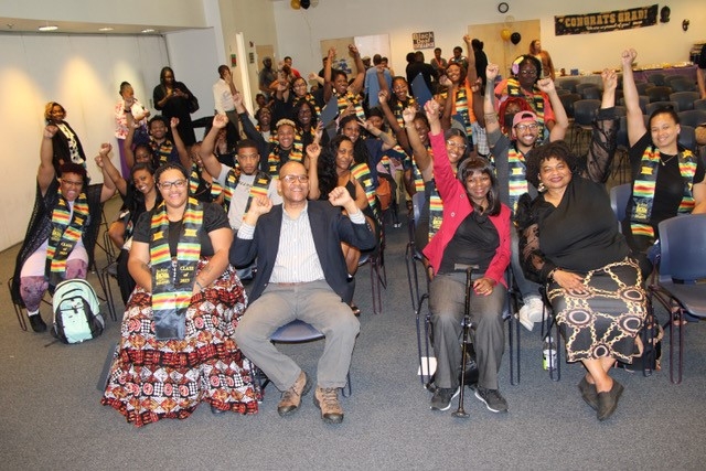 A group of Black students at Gallaudet University and the co-directors of the Center for Black Deaf Studies sit down raising their fists. 