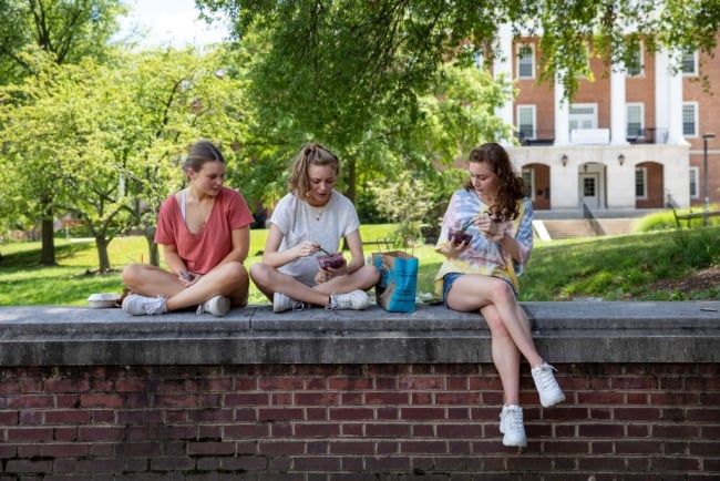Three young women eat outside of the University of Maryland campus in College Park, eating food from takeout containers